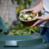 Close Up Of Woman Emptying Food Waste Into Garden Composter At Home